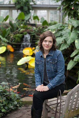 Sara Hays in a sunlit conservatory beside a koi pond